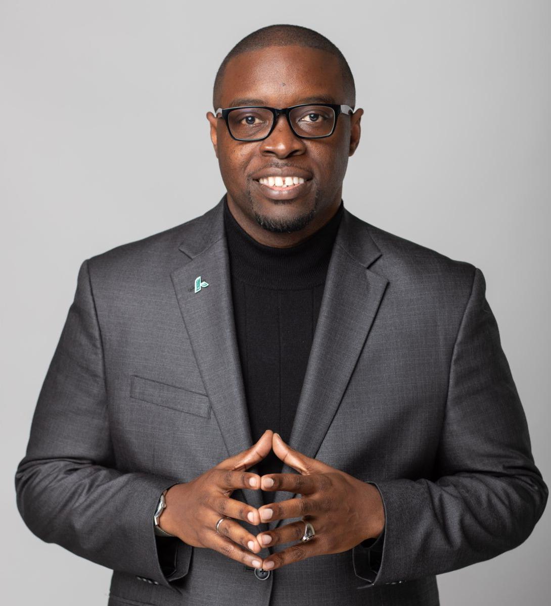 Dr. Jermaine Whirl, a smiling African American male, wearing a black suit with a white collared shirt, and black rimmed glasses. A round gold pin is on his left lapel.
